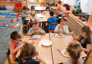 Dzieci siedzą przy stolikach i jedzą samodzielnie zrobione kanapki